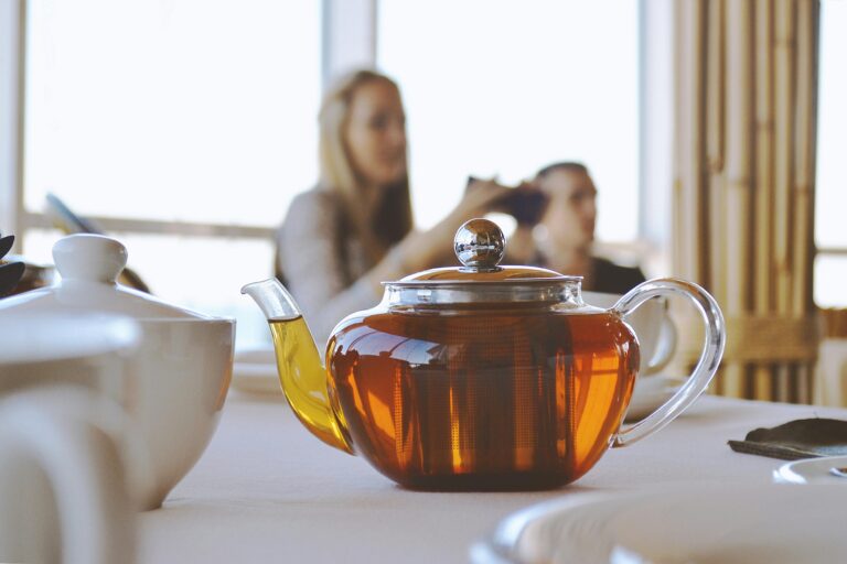Glass jug of tea on a counter with a woman blurred in the background