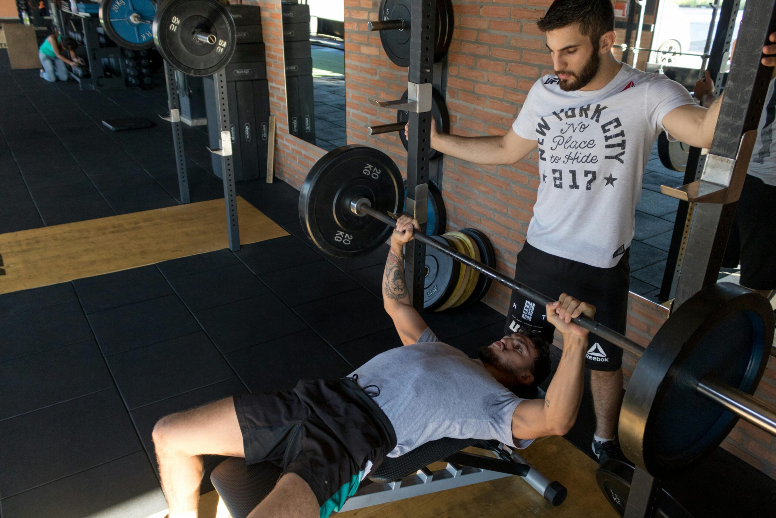 Men in the gym. One doing bench press and another watching