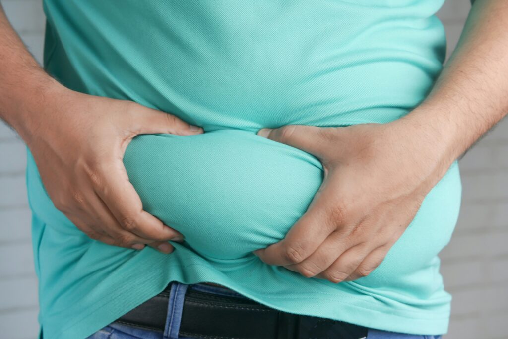 Person in a turquoise blue shirt grabbing their belly fat