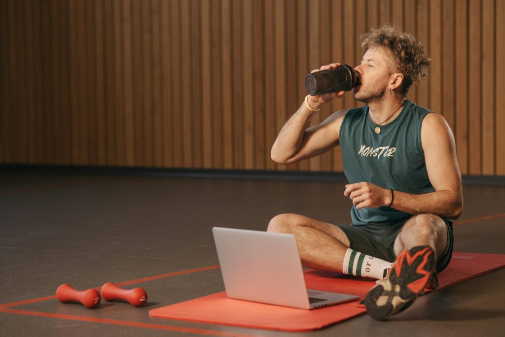man in the gym sitting on a yoga mat drinking from a cup